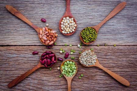 Close up  of various beans in wooden spoons setup on shabby wooden background.の写真素材