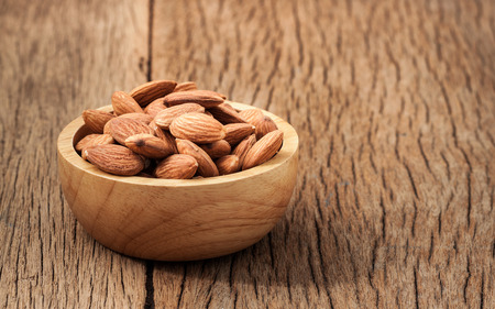 Closeup almonds kernels in wooden bowl with   on rustic wooden background .の写真素材