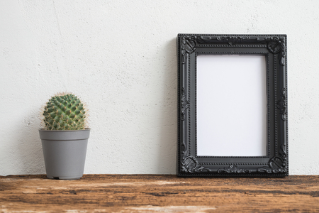 Black photo frame on old wooden table with cactus over white concrete wall backgroundの写真素材