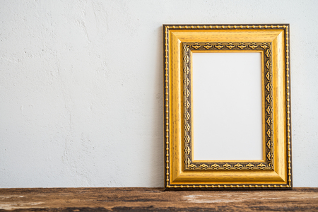 Golden vintage photo frame on old wooden table over white wall backgroundの写真素材
