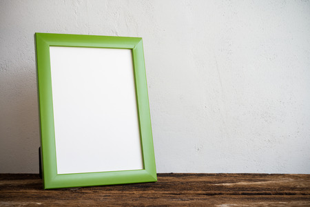 Green photo frame on old wooden table over white wall backgroundの写真素材
