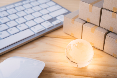 Online internet global purchases transportation business, cardboard boxes, glow earth global on table with keyboard and mouse, e-commerce online shopping and logistics shipping import export conceptの写真素材