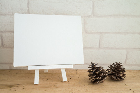 Blank white wooden easel  blank canvas and pine on wooden table with white wallpaper background for your textの写真素材
