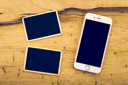 Smart phone and chalkboard on wooden table background - Vintage filter effectの写真素材