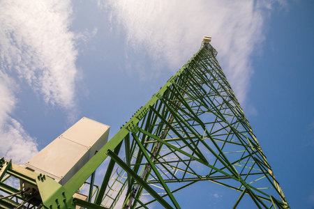 Green telecommunication tower against blue sky blue from bottom view