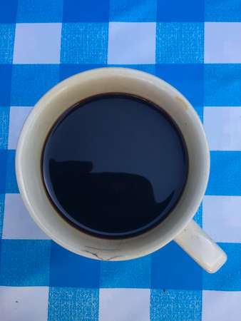 a white cup of black coffee on checked plastic tableclothの写真素材