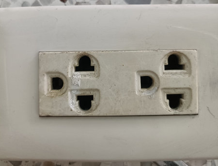 Close up of double electrical outlet with worn and dirty appearance, mounted on white surface,...