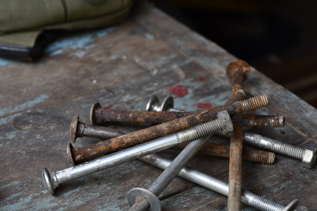 Old and rusty nails and bolts scattered on worn wooden surface, conveying sense of neglect and age, with rustic and industrial feelの写真素材