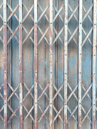 Rusty metal gate with crisscross pattern and peeling paint old and weathered surface blue and brown tones vertical and diagonal lines industrial style textured background vintage appearanceの写真素材