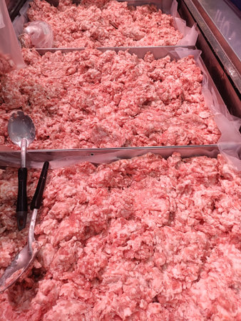 Raw ground meat display case grocery store or butcher shop pinkish color textured surface metal...