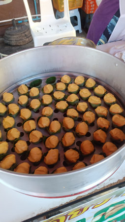 Steamed dessert in banana leaf cup with orange custard topping, street food vendor tray steaming multiple bite size sweets, warm colorful snack display, appetizing local treatの写真素材