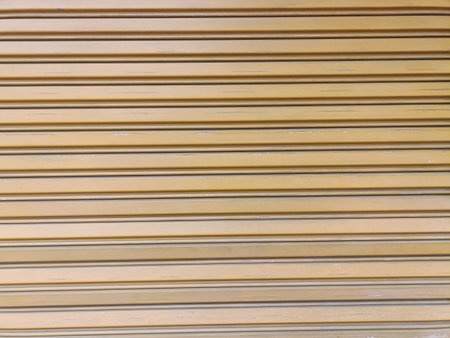 Sunlit beige metal roller shutter with horizontal ridged panels showing subtle wear and smooth...