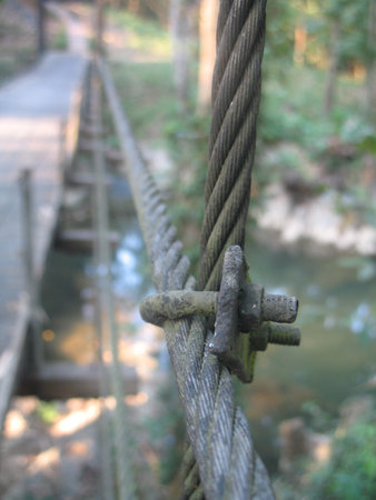 Weathered steel cable clamp on suspension bridge cable in forest, closeup showing worn metal texture...