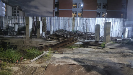 Abandoned construction site at night with corrugated metal fence, concrete pillars, scattered rebar...