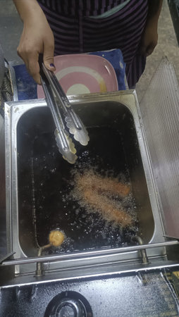 Street food fryer hot oil deep frying tongs hand night crispy snack with lively vibeの写真素材