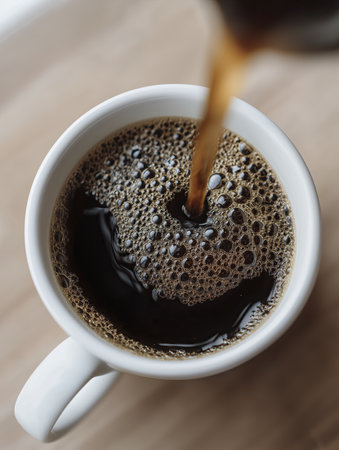 Fresh black coffee pouring into white ceramic cup creating bubbly crema and warm inviting aromaの素材