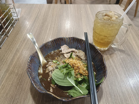 Noodle soup pork basil fried garlic chopsticks spoon iced tea on wooden table cozy savory comfort