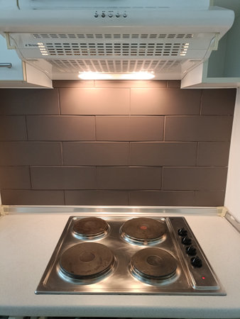 Stainless cooktop electric hob kitchen hood tile backsplash warm light modern kitchen clean counter cozy ambianceの写真素材