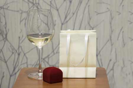Wine glass and red jewerly box on wooden table over grunge wall. Holiday background.の写真素材
