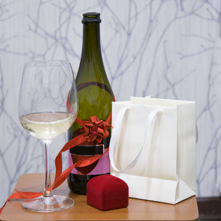 Wine glass, bottle decorated with ribbon bow. Jewelry box, holiday gift on woodern tableの写真素材