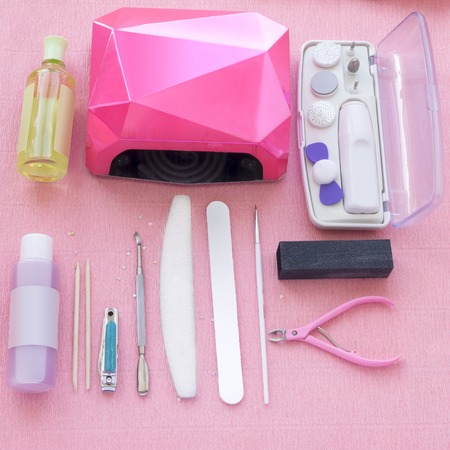 Gel manicure set with nail file, lamp, tweezers, wood sticks and accessories on pink background, top angle view.の写真素材