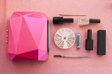 Manicure set for gel nail procedure: uv lamp, gel polishes and files on pink background.の写真素材