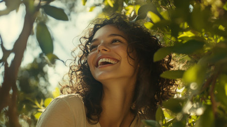 A cheerful woman with curly hair surrounded by greenery, showcasing her vibrant personality and connection to nature in a sunny outdoor settingの素材