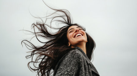 A dynamic shot of a woman with a playful expression, caught mid-laugh, with wind blowing through her hair, capturing the essence of spontaneity and joy.の素材