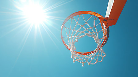 A high-angle view of a basketball hoop and net against a clear blue sky, with the sun shining brightly and casting shadows on the court belowの素材