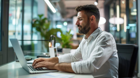 A businessman reviewing financial reports on a wireless laptop in a modern office space, leveraging technology for data-driven decision-making.の素材