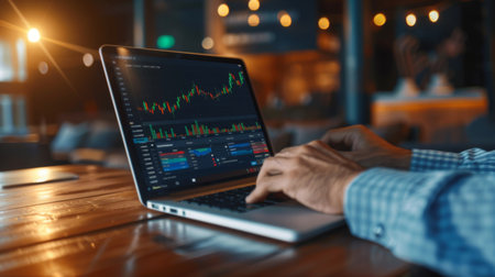 A businessman making online payments on a laptop, with financial transaction graphs displayed on the screen.の素材