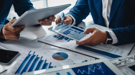A financial advisor discussing investment options with a client, pointing to charts and graphs on a tablet in a modern officeの素材