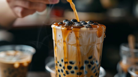 A hand stirring a glass of brown sugar bubble milk tea, the rich caramel hue swirling with the creamy base, promising a decadent treat for the taste budsの素材