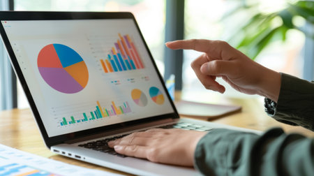 A close-up of a person's hand pointing at a colorful pie chart on a laptop screen during a meeting.の素材