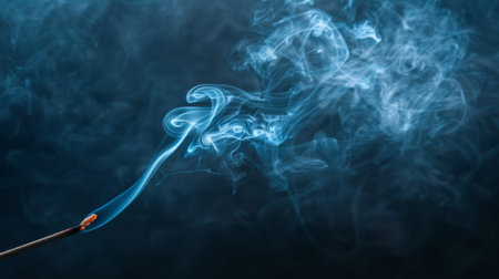 Close-up of a burning incense stick with wisps of smoke curling in the air.の素材