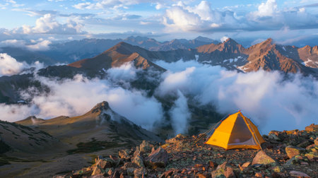 A tent pitched on a mountain ridge with a view of clouds rolling over nearby peaksの素材