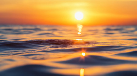 A close-up of the sun setting over a calm sea, with the golden and orange hues reflecting on the watera surface, creating a serene and picturesque sceneの素材
