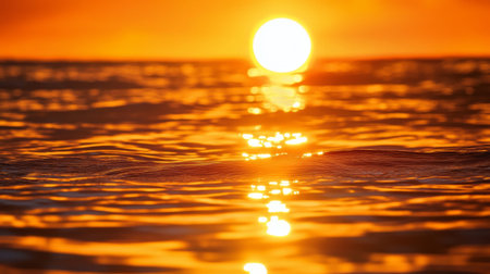 A close-up of the sun setting over a calm sea, with the golden and orange hues reflecting on the watera surface, creating a serene and picturesque sceneの素材