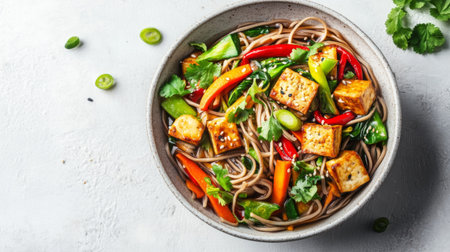 A bowl of noodles with a variety of vegetables and tofu, artistically presented on a white surface, showcasing a healthy and appetizing dish with vibrant colors.の素材