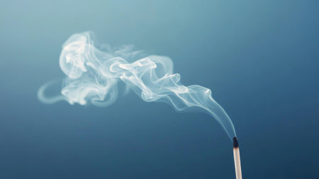 A close-up of wisps of white smoke rising from a burning incense stick, swirling gently in the air, symbolizing calmness, spirituality, and meditation.の素材