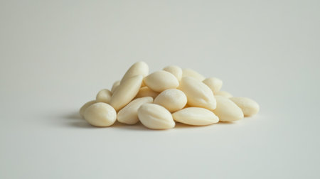 A close-up of a handful of blanched almonds on a white background, highlighting their smooth surface and pale color in a clean, minimalist setting.の素材