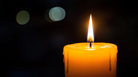 A single burning candle illuminates the darkness, creating a serene atmosphere. The warmth and gentle flicker evoke feelings of peace and tranquility.の素材