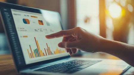 A close-up view of a hand pointing at data charts on a laptop screen. This image captures the essence of business analytics and data-driven decision-making.の素材