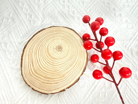 A beautiful wooden slice paired with a striking red berry branch creates a stunning contrast against a textured white background, perfect for seasonal themes.の写真素材