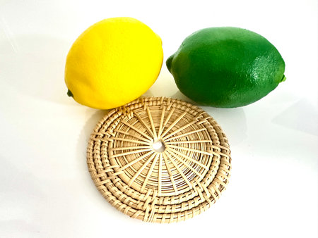 Vibrant yellow lemon and bright green lime sit atop a round woven basket on a clean white surface, showcasing a fresh and inviting kitchen aesthetic perfect for any food lover.の写真素材