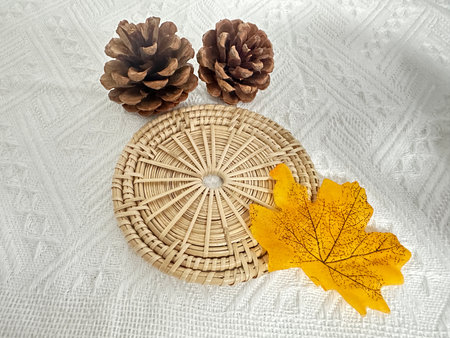 A captivating arrangement featuring two pine cones, a vibrant yellow leaf, and a woven basket on a textured fabric background, perfect for inspiring rustic decor.の写真素材