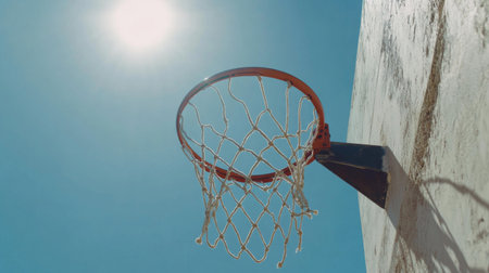 A vibrant basketball hoop stands out against a bright blue sky, highlighting the excitement of outdoor sports and the energy of an active lifestyle under warm sunlight.の素材