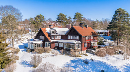 A picturesque Nordic-style house with a sloping roof, surrounded by snow-covered trees and a serene winter landscape under a clear blue skyの素材