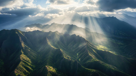 An aerial view of expansive mountain ranges with sharp peaks and deep valleys, as sunlight streams through the clouds, illuminating the rocky terrain.の素材