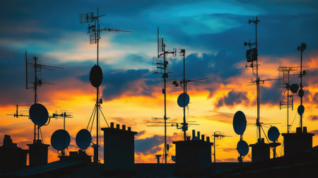 A stunning silhouette of various antennas against a vibrant sunset sky, showcasing the intersection of technology and nature in an urban setting.の素材